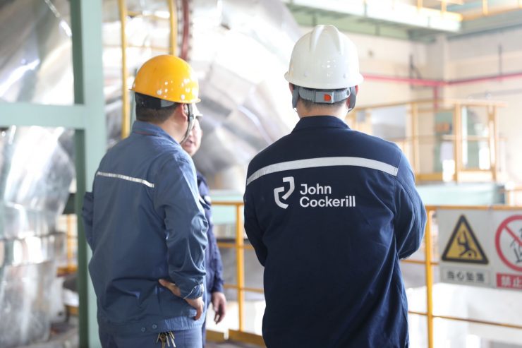 two men from behind wearing a helmet in a steel plant