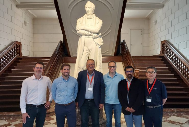 six men posing in front of a John Cockerill statue and a large double staircase in a castle